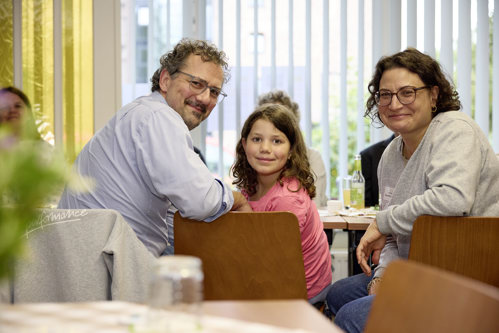 Eine Familie mit einem Kind sitzt am Tisch und schaut zur Kamera